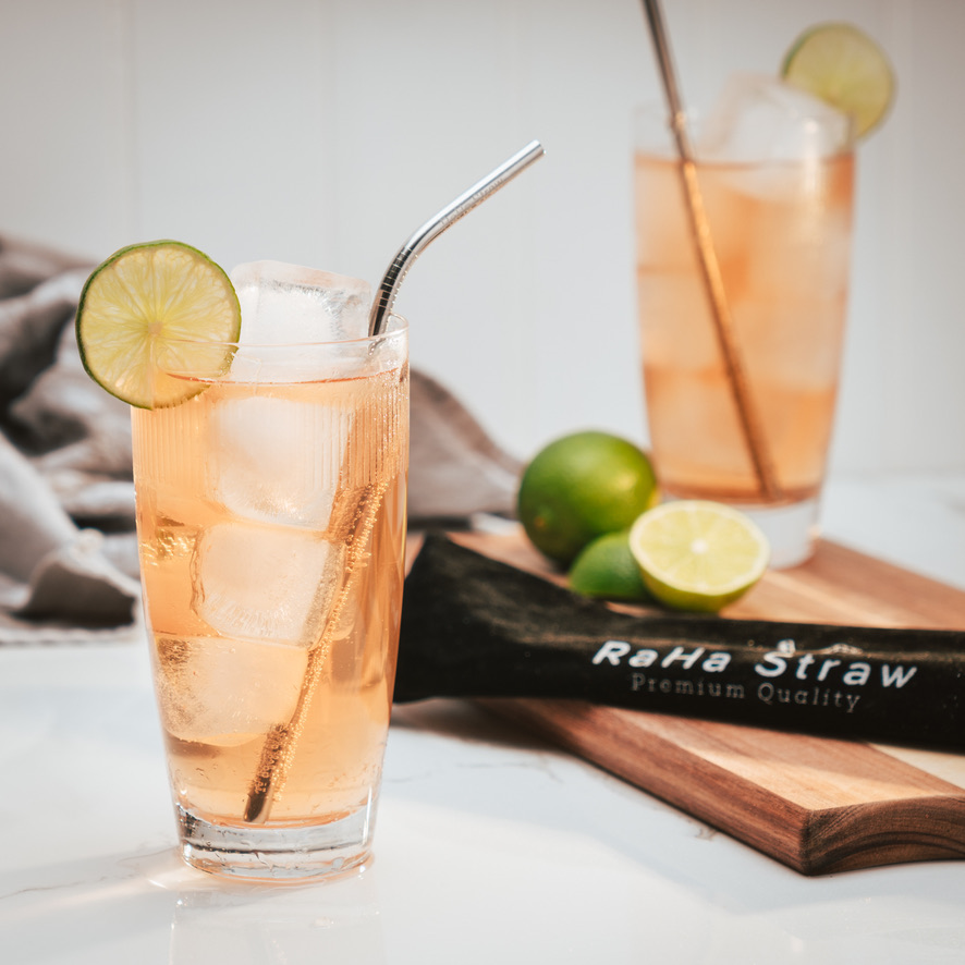 A RaHa Straw stainless steel straw resting in a glass of iced tea garnished with lime