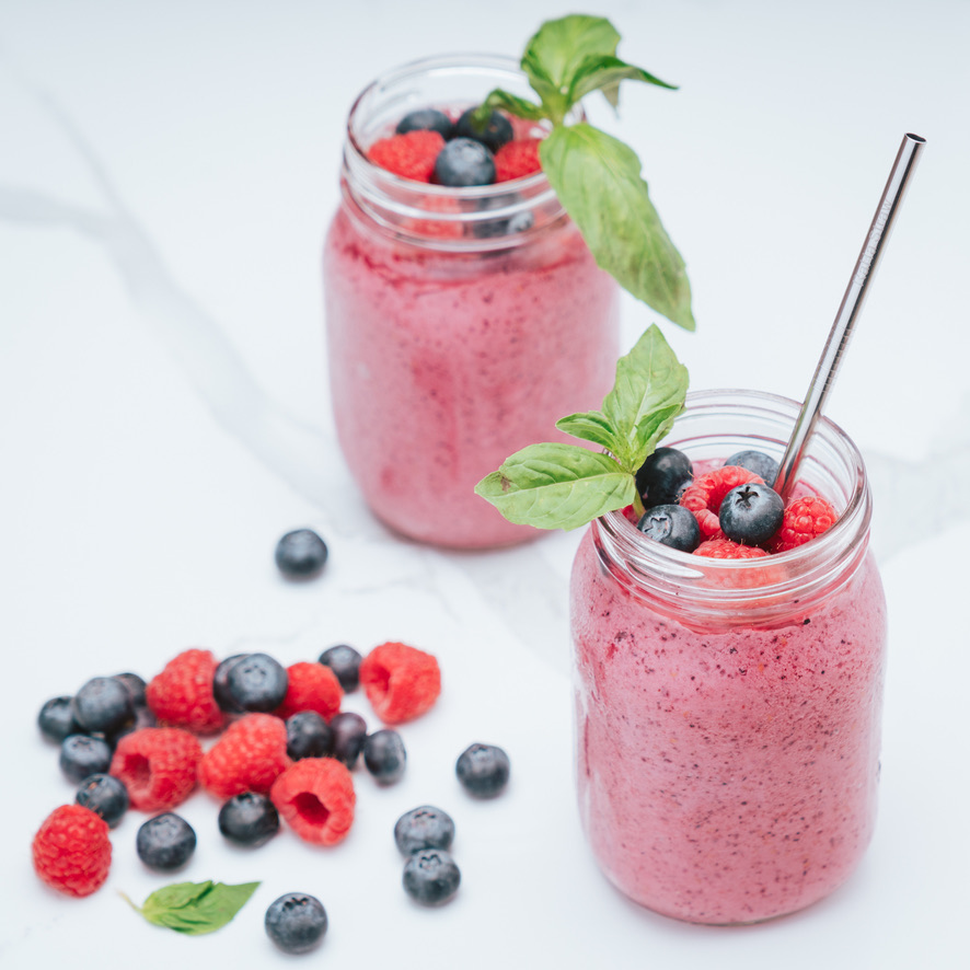 A RaHa Straw stainless steel straw in a mixed berry smoothie topped with raspberries, blueberries, and basil